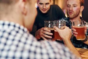 glädjande förbi knackar öl glasögon. grupp av människor tillsammans inomhus i de pub ha roligt på helgen tid foto