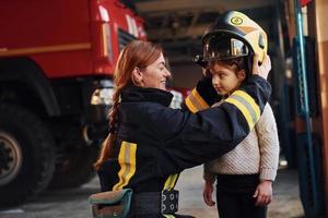 Lycklig liten flicka är med kvinna brandman i skyddande enhetlig foto