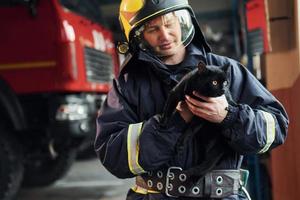 porträtt av brandman i skyddande enhetlig den där innehar söt liten svart katt foto