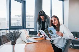 två kvinnor i formell kläder är inomhus i de modern kontor Arbetar tillsammans foto