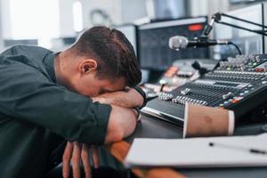 trött förbi arbete. ung man är inomhus i de radio studio är upptagen förbi utsända foto