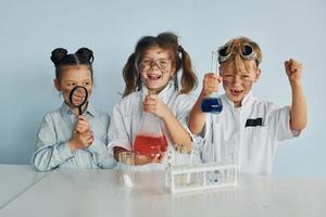 Lycklig vänner leende. barn i vit rockar spelar en vetenskapsmän i labb förbi använder sig av Utrustning foto