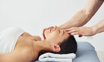 huvud massage. ung kvinna är liggande ner när man håller på med procedur till henne i spa foto