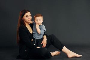 Sammanträde på de golv. mor i eleganta svart kläder är med henne liten son i de studio foto