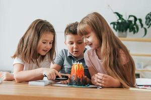 byggnad vulkan från plasticine. barn har roligt i de inhemsk rum på dagtid tillsammans foto