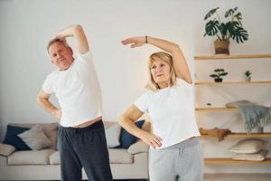 håller på med stretching. senior man och kvinna är tillsammans på Hem foto