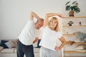 håller på med stretching. senior man och kvinna är tillsammans på Hem foto