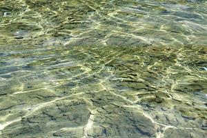 defokusering suddig transparent blå färgad klar lugna vatten yta textur med stänk och bubblor. trendig abstrakt natur bakgrund. vatten vågor i solljus med kopia Plats. blå vattenfärg lysande foto