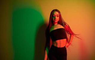 mot vägg. modern ung kvinna stående i de studio med neon ljus foto