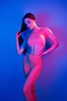 visar kropp. modern ung kvinna stående i de studio med neon ljus foto
