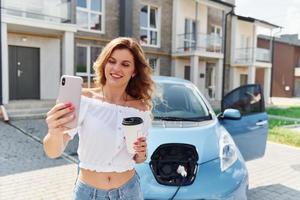 med kopp av dryck. ung kvinna i tillfällig kläder med henne elektromobil utomhus på dagtid foto