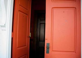 gammal trä röd dubbel- dörrar ledande i till en mörk hall foto