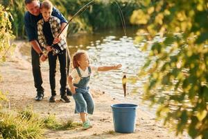 flicka sätta fisk in i de hink. far med son och dotter på fiske tillsammans utomhus på sommartid foto