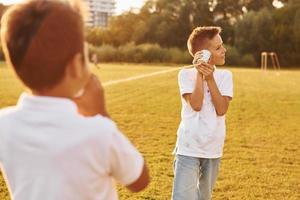 två Pojkar har roligt förbi använder sig av tenn kan telefon på de sportigt fält foto