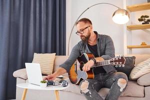 på de soffa. spelar akustisk gitarr. man i tillfällig kläder är inomhus foto