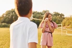 pojke med flicka har roligt förbi använder sig av tenn kan telefon medan stående utomhus på de fält foto