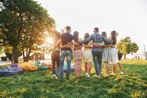 se från Bakom. grupp av ung människor ha en fest i de parkera på sommar dagtid foto