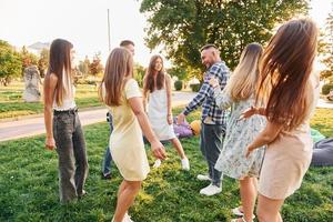 Lycklig helgen tid utgifter. grupp av ung människor ha en fest i de parkera på sommar dagtid foto