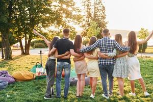 se från Bakom. grupp av ung människor ha en fest i de parkera på sommar dagtid foto