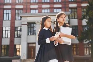 innehav böcker. två skol är utanför tillsammans nära skola byggnad foto