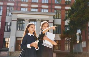 innehav böcker. två skol är utanför tillsammans nära skola byggnad foto