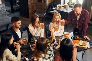 positiv ansiktsbehandling uttryck. grupp av ung vänner Sammanträde tillsammans i bar med öl foto