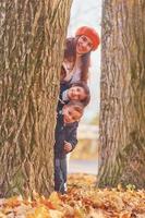 dölja Bakom träd. mor med henne liten son och dotter är har roligt i de höst parkera foto