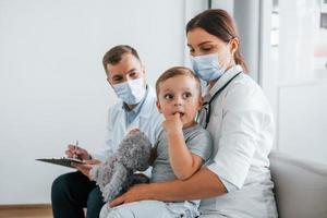 liten pojke är i de klinik. två doktorer i vit rockar är i de sjukhus arbetssätt tillsammans foto