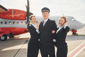 pilot och två flygvärdinnor. besättning av flygplats och plan arbetare i formell kläder stående utomhus tillsammans foto