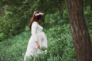 i skogen. vacker gravid kvinna i klänning har en promenad utomhus. positiv brunett foto