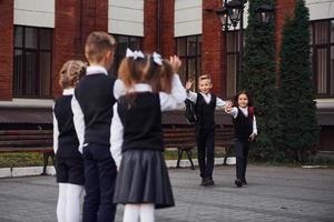 ha en möte. grupp av barn i skola enhetlig den där är utomhus tillsammans nära utbildning byggnad foto