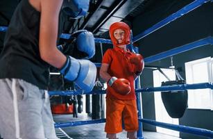 två Pojkar i skyddande Utrustning ha sparring och stridande på de boxning ringa foto