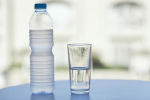 flaska av vatten och glas av vatten på tabell i varm sommar dag, närbild foto