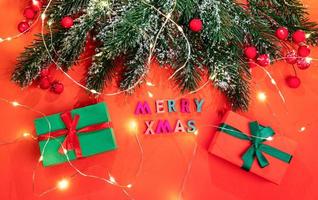 xmas hälsning kort med gran grenar, snö, bär, jul lampor, gåva lådor med Färg brev glad xmas på röd. foto