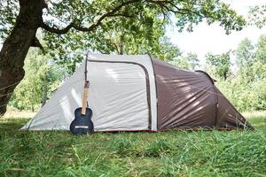 akustisk gitarr nära en camping tält i skog foto