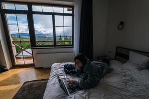 ung kvinna arbetssätt på bärbar dator medan liggande på säng foto