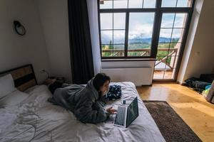 ung kvinna arbetssätt på bärbar dator medan liggande på säng foto
