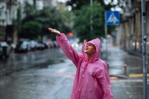 ung leende kvinna med regnkappa medan njuter en regnig dag. foto