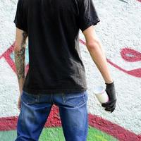 en ung ligist med en spray kan står mot en betong vägg med graffiti målningar. olaglig vandalism begrepp. gata konst foto