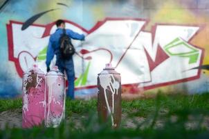 en få Begagnade måla burkar mot de bakgrund av de Plats med de vägg på som de ung kille drar en stor graffiti teckning. modern konst av teckning väggar i graffiti foto