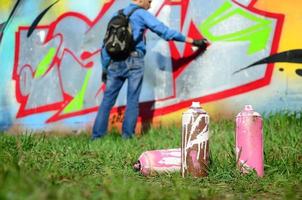 en få Begagnade måla burkar mot de bakgrund av de Plats med de vägg på som de ung kille drar en stor graffiti teckning. modern konst av teckning väggar i graffiti foto