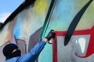 en ung ligist med en dold ansikte målarfärger graffiti på en metall vägg. olaglig vandalism begrepp foto