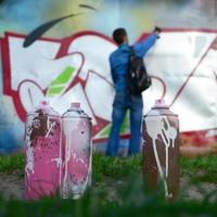 en få Begagnade måla burkar mot de bakgrund av de Plats med de vägg på som de ung kille drar en stor graffiti teckning. modern konst av teckning väggar i graffiti foto