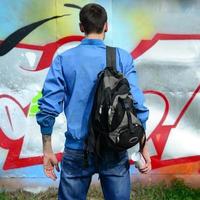 en ung graffiti konstnär med en svart väska utseende på de vägg med hans graffiti på en vägg. gata konst begrepp foto