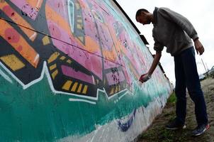 en ung kille i en grå luvtröja målarfärger graffiti i rosa och grön c foto