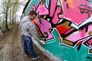 en ung kille i en grå luvtröja målarfärger graffiti i rosa och grön c foto