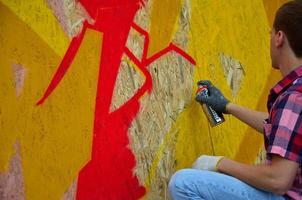 en ung rödhårig graffiti konstnär målarfärger en ny graffiti på de vägg. Foto av de bearbeta av teckning en graffiti på en vägg närbild. de begrepp av gata konst och olaglig vandalism