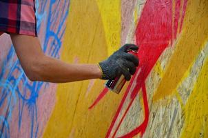 en hand med en spray kan den där drar en ny graffiti på de vägg. Foto av de bearbeta av teckning en graffiti på en trä- vägg närbild. de begrepp av gata konst och olaglig vandalism