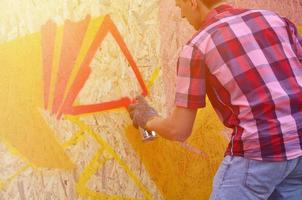 en ung rödhårig graffiti konstnär målarfärger en ny graffiti på de vägg. Foto av de bearbeta av teckning en graffiti på en vägg närbild. de begrepp av gata konst och olaglig vandalism