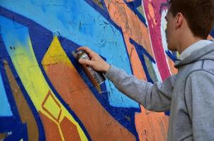 en ung rödhårig graffiti konstnär målarfärger en ny graffiti på de vägg. Foto av de bearbeta av teckning en graffiti på en vägg närbild. de begrepp av gata konst och olaglig vandalism